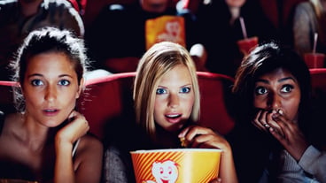 Wow popcorn and women in the theater watching a movie for pleasure while eating a snack facial expressions and eating with shocked young friends in a theater audience to experience a movie together