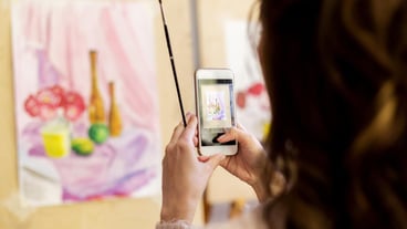 technologyl, creativity and people concept - woman artist or student with smartphone and brush photographing still life painting or picture at art school studio