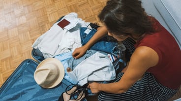 Summer vacation, travel, tourism and objects concept - close up of woman packing travel ba