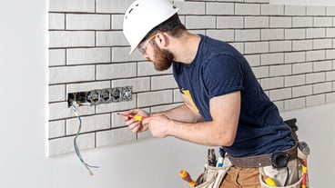 Electrician construction worker with a beard in overalls during the installation of sockets. Home renovation concept.