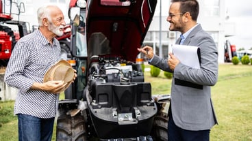 Tractor dealer presenting agricultural machines and modern engine to the farmer at dealership