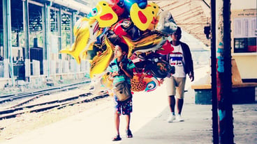 Full length of boy selling multi colored balloons on railroad station platform
