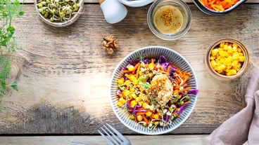 Vegetable salad of fresh red cabbage with carrots, onions, corn, mung seedlings in a plate on wooden background. Selective focus. Top view. Copy space.