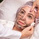 Woman is lying in the cosmetologist s office on the procedure of moisturizing her face. The cosmetologist applies a moisturizing mask to the patient's face.
