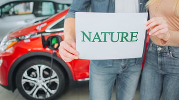Young family buying first electric car in the showroom. Green car. Close-up of hands holding paper with word Nature on battery electric car background. Environment protection.