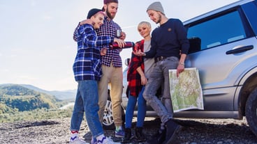 Summer travel concept. Happy friends using paper map near rented car in nature.