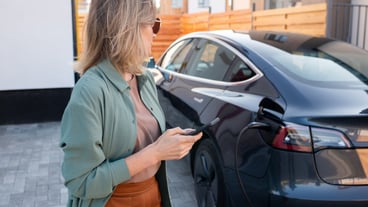 Yong elegant woman with smartphone looking at her electric car
