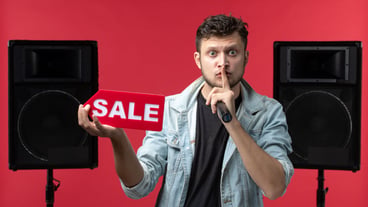 Front view of male singer performing on stage holding sale writing on red wall