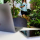 Businesswoman holding coffee cup and smartphone walking from home room to working desk in corner small garden with laptop and tablet computer. Concept of new normal people and work at home.