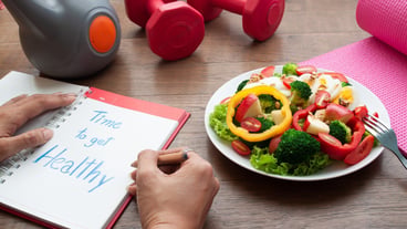 Woman writing on diary book with salad and fitness equipments on table