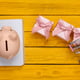 Concept, economy, shopping list. Piggy bank with grocery cart, gift boxes, notebook on yellow wooden surface. View from above