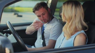 Young woman and driving school instructor with clipboard talking in car Woman listening to instructor in car learning to drive