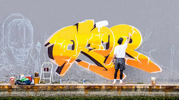 Street artist painting colored graffiti on public space wall