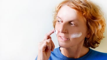 Smiling elderly woman applying cream to her face while sitting against the wall
