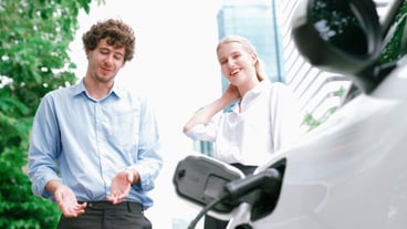 A progressive businessman and businesswoman install a charging port from the charging station onto their electric car before driving through the city center – an environmentally friendly, rechargeable car powered by clean energy.