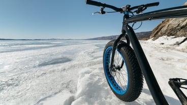 Fatbike (also called fat bike or fat-tire bike) - Cycling on large wheels. Teen rides a bicycle through the snow mountains in the background.