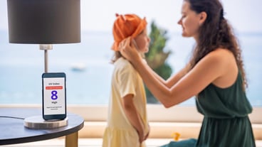Mother puts sun hat on daughter as smartphone displays high uv alert practical response to sun