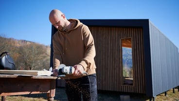 Bald male worker cutting metal using circular saw while building wooden frame house