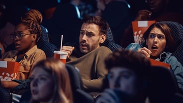 A group of friends watching a horror movie at the cinema.