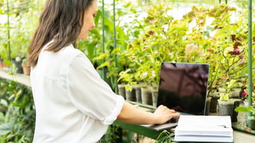 Young business woman gardener using laptop in greenhouse. Latest technology in the gardening business.