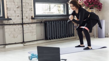Fitness girl training with rubber band and look sport tutorial Smiling fit sports woman in sport clothes in room watching fitness videos on laptop