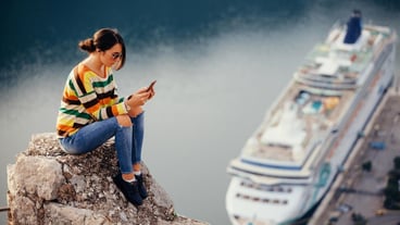 Full length of young woman using phone while sitting on retaining wall against lake