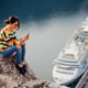 Full length of young woman using phone while sitting on retaining wall against lake