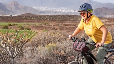 Sporty senior woman in outdoors excursion on her electro bike  Green vineyard and mountain in background
