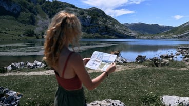 A white girl looks at a map near a quiet lake in nature, Covadonga, Asturias, Spain.