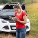 Portrait of young stressed woman standing at broken car and reading owner manual