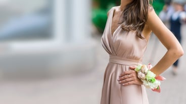 Beautiful bridesmaid in a silk dress with a flower boutonniere on her hand against a green garden