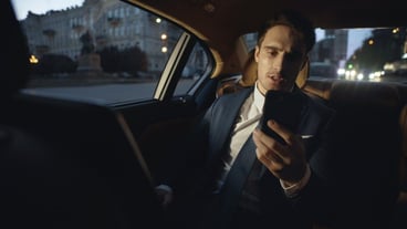 Tired male professional speaking on video call on smartphone in dark luxury car