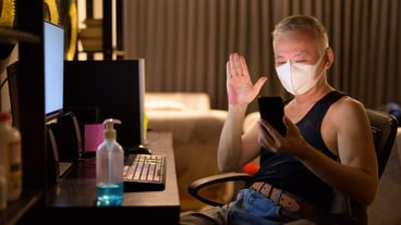 Mature Japanese man with mask video calling with phone while working overtime at home