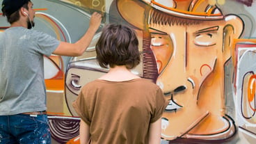 Rear view of a woman looking at an artist doing graffiti on the wall