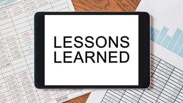 Tablet with text LESSONS LEARNED on your desktop with documents, reports and graphs. Business and finance concept