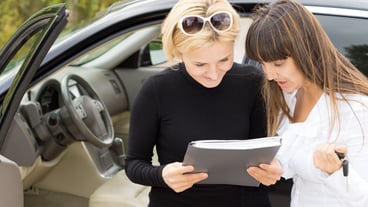 Blond woman smiling as she reads a contract for the purchase of her new car