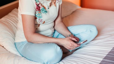 Low section of woman using mobile phone on bed at home