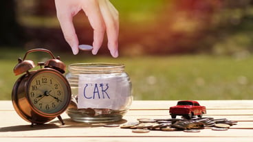Close-up of hand putting coin in jar with alarm clock on table