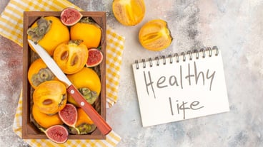 Top view delicious persimmons and cut figs in wood box yellow kitchen towel healthy life written on notebook