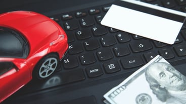 Credit card, dollar and red toy car on laptop keyboard.