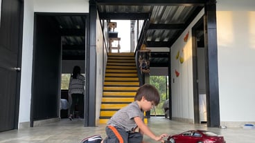 Side view of boy kid playing on the floor with car toy red color house stairs behind