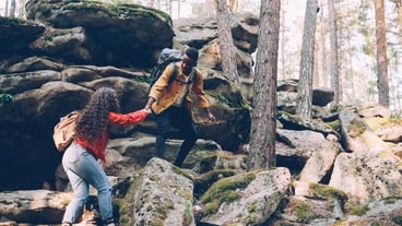 Multiethnic young couple hiking up a mountain African American man giving woman a hand to help her pull up People are carrying backpacks