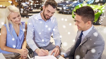 Car business, sales and people concept - happy couple with a dealership buying a car and signing documents at a car show or in a hall on a snow effect