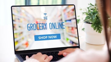 Hand using laptop computer with grocery online shopping over blur supermarket on screen background