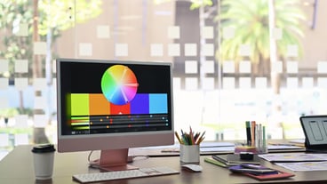 Design studio with computer color swatches and wireframe sketches for mobile application on wooden table