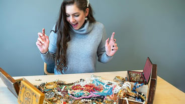 Slim brunette sitting at the table with lots of jewelry choosing and trying different jewelry