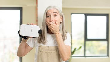 pretty senior woman covering mouth with a hand and shocked or surprised expression with vr goggles