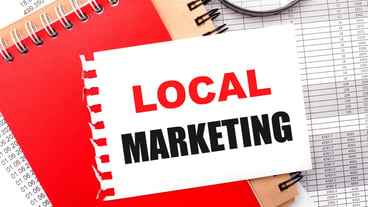 On a light background reports a magnifying glass brown and red notepads and a white notepad with the text LOCAL MARKETING Business concept