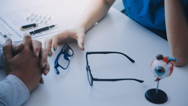 Closeup of Asian female doctor talking with elderly patient showing eyeball model and explaining eye disease in hospital