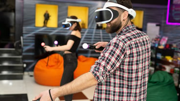 Friends, a man and a woman use a virtual reality headset with glasses and hand motion controllers in the play area. Modern technologies concept image.